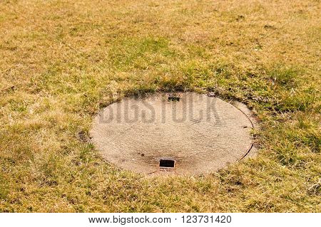 Concrete manhole cover drainage system in the midst of cropped grass