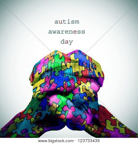 text autism awareness day and the hands of a man put together patterned with many puzzle pieces of different colors, with a slight vignette added