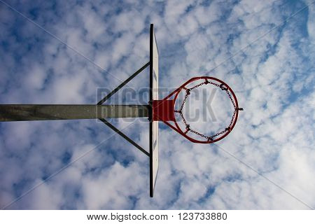 Old neglect basketball backboard with rusty hoop above street court. Blue sky in background.