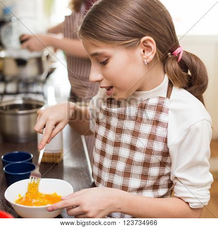 Small Girl In Apron Whisking Eggs In White Bowl