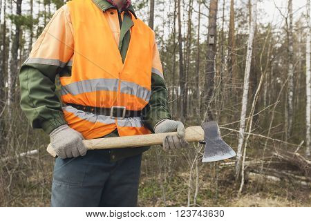 Lumberjack with an axe in the hands of the forest backdrop. One worker in special clothes in the foreground.