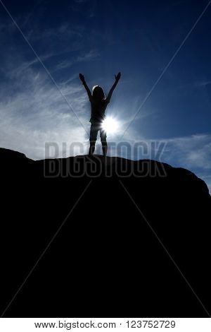 Silhouette of hiker at the top of a peak with blue sky in background