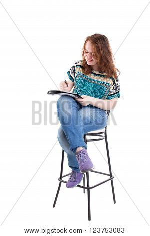 Beautiful smiling redhead plus size wreckled model with folder and ballpoint pen sitting on the bar chair. Isolated on a white background.