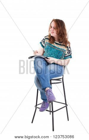 Beautiful smiling redhead plus size wreckled model with folder and ballpoint pen sitting on the bar chair. Isolated on a white background.