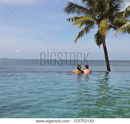 Young couple relaxing in infinity pool under coco palms in front of tropical landscape