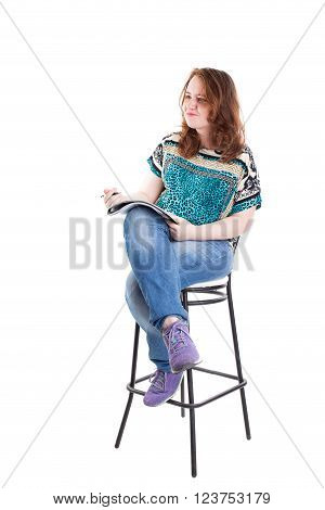 Beautiful smiling redhead plus size wreckled model with folder and ballpoint pen sitting on the bar chair. Isolated on a white background.