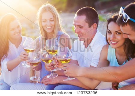 People holding glasses of white wine making a toast at the beach picnic