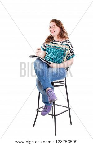 Beautiful smiling redhead plus size wreckled model with folder and ballpoint pen sitting on the bar chair. Isolated on a white background.