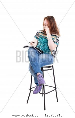 Beautiful smiling redhead plus size wreckled model with folder and ballpoint pen sitting on the bar chair. Isolated on a white background.