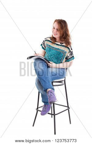 Beautiful smiling redhead plus size wreckled model with folder and ballpoint pen sitting on the bar chair. Isolated on a white background.