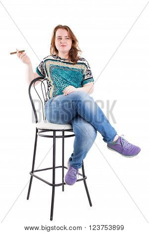 Smiling redhead plus size wreckled model sitting on the bar chair with cigar. Studio shot. Isolated on a white background.