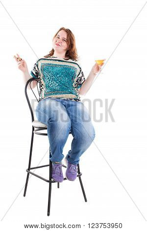 Smiling redhead plus size wreckled model sitting on the bar chair with glass of whiskey and cigar. Studio shot. Isolated on a white background.