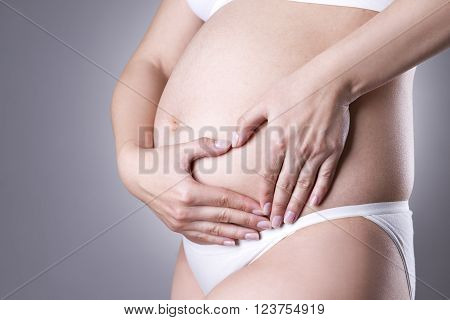 Caucasian pregnant woman in white lingerie with abdominal pain on gray studio background. Pregnancy concept