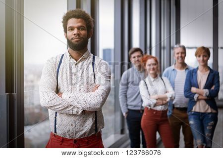 Corporate portrait of young black hipster businessman with his colleagues in background. Post processed with vintage film and sun filter.