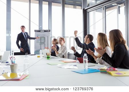 Business man showing ground-plan during meeting in modern office while his colleagues cheering.