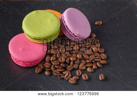 Colorfull macaroons with roasted coffee beans on slate