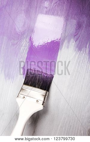 Painting white wooden surface with white paintbrush and violette of lavender color.