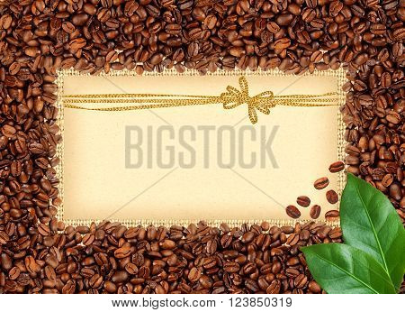 Spilled coffee beans frame over burlap textile with greeting card with golden bow