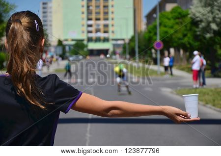 Young girl hold cup of water during roller skating competition and helping the athletes to hydrate yourself during the race