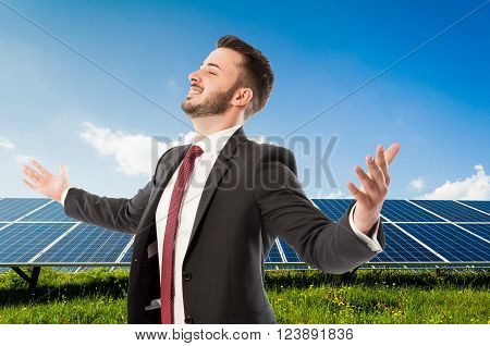 Happy smiling businessman with wide outspread or outstretched arms on solarpower photovoltaic panel background