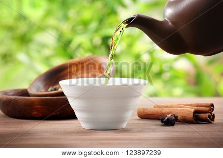 Pouring green tea into white pialat on wooden table