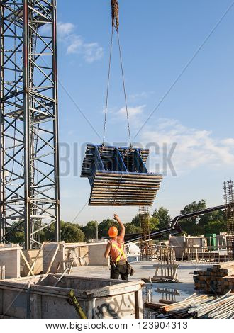 Construction worker receiving a stack of scaffolding pieces from a crane on a construction site