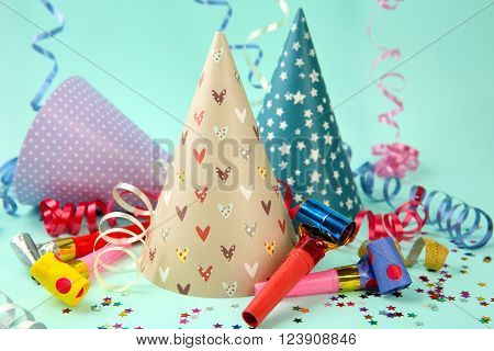 Three Birthday hats with serpentine streamer and noise makers on light blue background