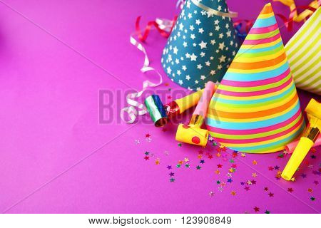 Birthday hats with serpentine streamer and noise makers on purple background