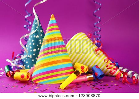 Three Birthday hats with serpentine streamer and noise makers on purple background