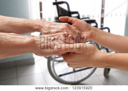Hands of an elderly man holding the hand of a woman on wheelchair background