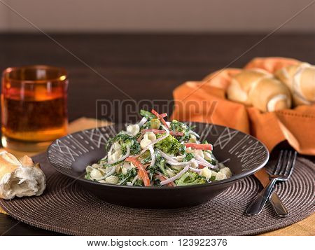 Pasta salad with vegetables served in brown ceramic bowl on textural dark brown place mat