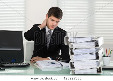 Businessman Suffering From Neckache With Invoice On Desk