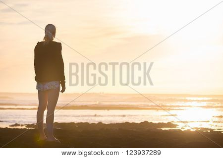 Silhouette of casualy dressed sporty woman watching sunset at the beach.
