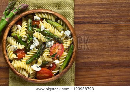 Baked green asparagus, cherry tomato, blue cheese and rotini pasta salad served in wooden bowl, photographed overhead on dark wood with natural light (Selective Focus, Focus on the top of the salad)