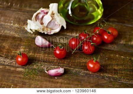 closeup of some cherry tomatoes, some garlic cloves and a glass cruet with olive oil on a rustic wooden table