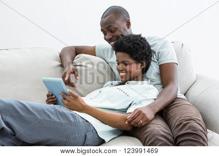Pregnant couple using digital tablet on sofa in living room