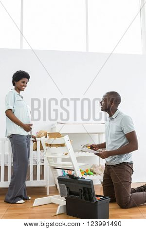 Pregnant woman looking at man fixing a baby chair at home
