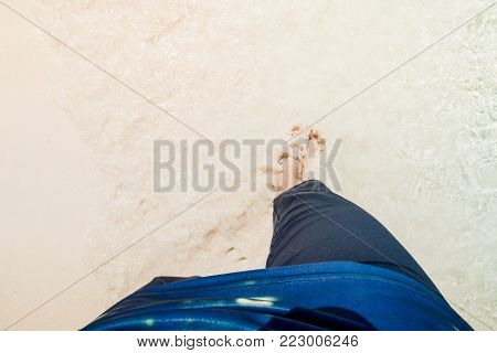 Point of view looking down people walking on the beach with barefoot and wave of water over feet in sunny day.Summer vacation concept.Relax time
