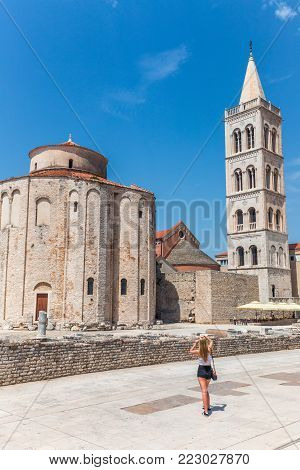 Blond girl is photographing monuments of historic center of the Croatian town of Zadar at the Mediterranean Sea, Europe.