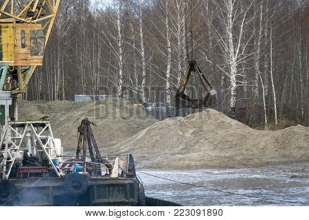 The motor grader aligns the dirt road. A bulldozer on wheels moving with a bucket. The wheel tractor moves the gravel with a bucket. Blue sky and white clouds in the background