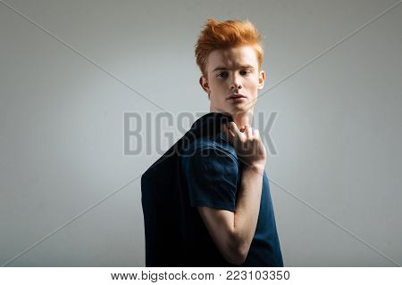 Look. Handsome humourless red-haired young man carrying a black jacket on his shoulder and thinking and looking over his shoulder