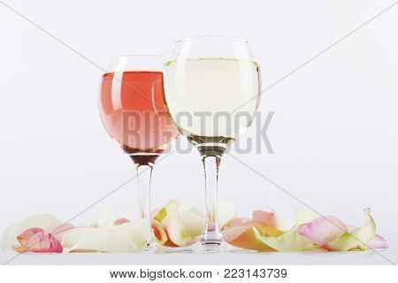 Glasses of rose and white wine surrounded by rose-petals on light background