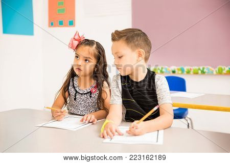 Good looking little kid trying to cheat on a math assigment in a preschool classroom