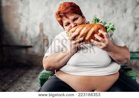 Fat woman sits in chair and eats sandwich, bulimic