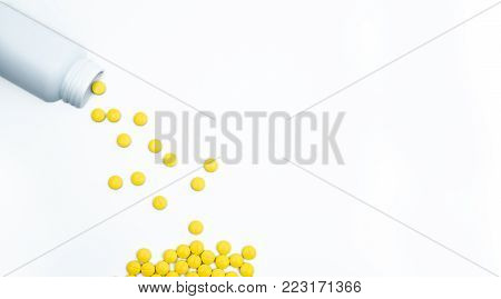 Yellow film coated tablets pills spilling out of pill bottle on white background with copy space. Painkiller tablet pills. NSAIDs pills for muscle pain.