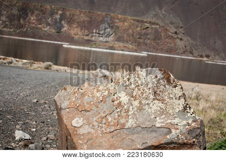 Close up of a rock in the desert with a blurry river and cliff in the background.