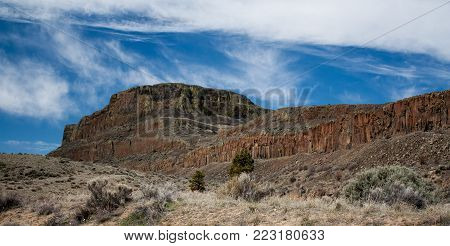 Red rocky desert ridge under a blue sky with clouds.