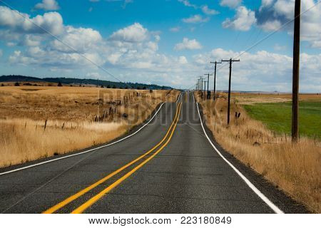 Country road going off in to the distance with a blue cloudy sky.