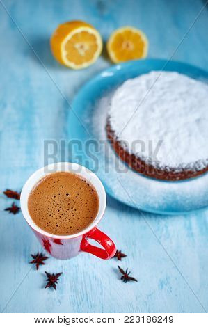 whole biscuit sprinkled with powdered sugar on the blue plate and two red cups of coffee, cut lemon and badon on blue wooden background