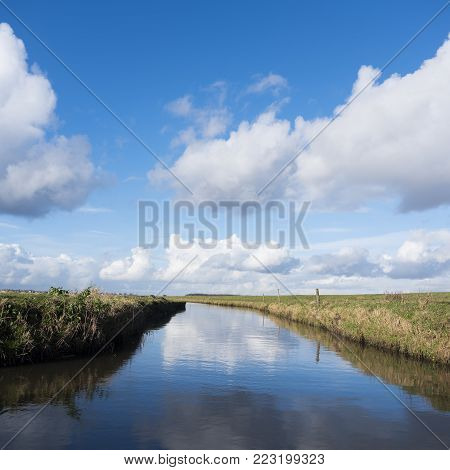 meadow landscape with canal and blue sky with clouds in the netherlands